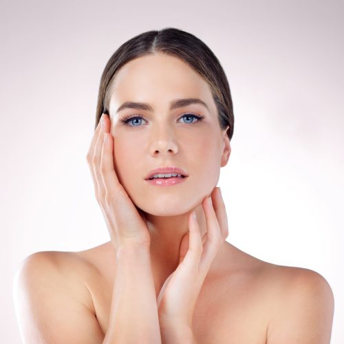 Beauty, skincare and portrait of woman with makeup, glow or wellness isolated on studio background. Cosmetic, hands or confident model touch face in spa for dermatology, health or shine for aesthetic.