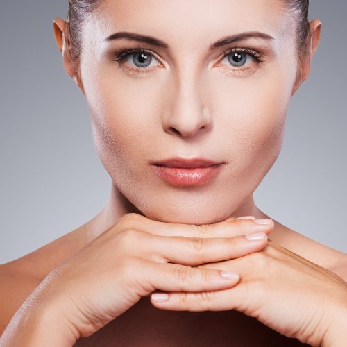 Fresh and beautiful. Portrait of shirtless mature woman looking at her shoulder while standing against grey background