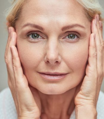Portrait of beautiful middle aged caucasian woman looking at camera with hands near face, close up. Beauty, skincare and cosmetology concept