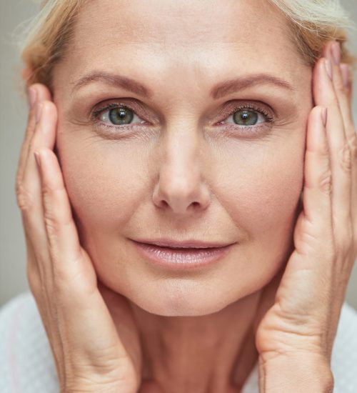 Portrait of beautiful middle aged caucasian woman looking at camera with hands near face, close up. Beauty, skincare and cosmetology concept