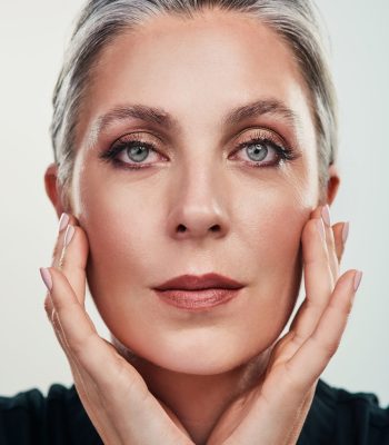 Portrait, mature and woman with makeup by white background for cosmetics, beauty and dermatology. Collagen, anti aging and skincare for fine lines, shine and glow in studio with female person.