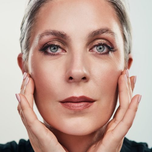 Portrait, mature and woman with makeup by white background for cosmetics, beauty and dermatology. Collagen, anti aging and skincare for fine lines, shine and glow in studio with female person.