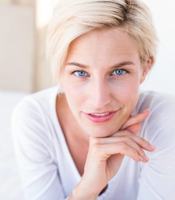 Smiling blonde woman lying on the bed and looking at camera in her bedroom