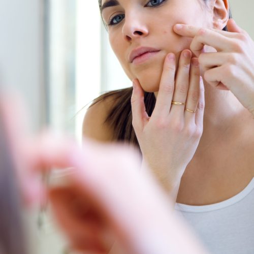 Portrait of woman caring of her beautiful skin on the face standing near mirror in the bathroom.